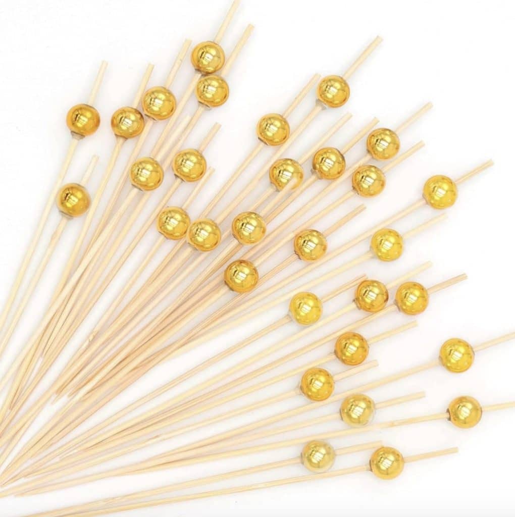 A collection of wooden skewers with shiny gold decorative spherical tips, perfect for elevating your New Year's recipes, arranged in a fan shape on a white background.